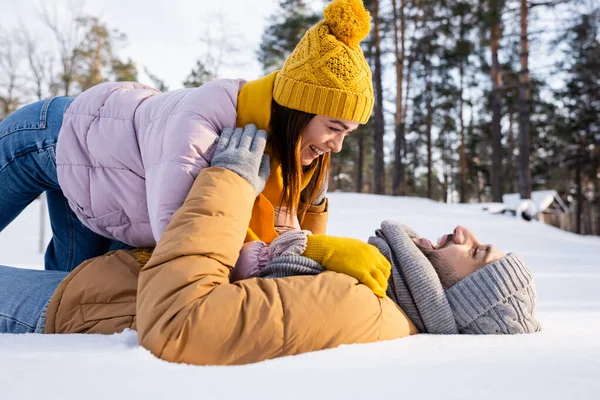 Вид сбоку веселого мужчины, лежащего на снегу рядом с девушкой в зимнем наряде — стоковое фото