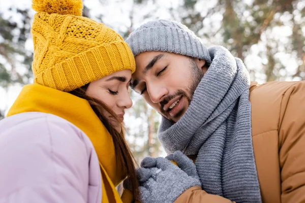 Coppia sorridente con gli occhi chiusi che si tiene per mano nel parco invernale — Foto stock