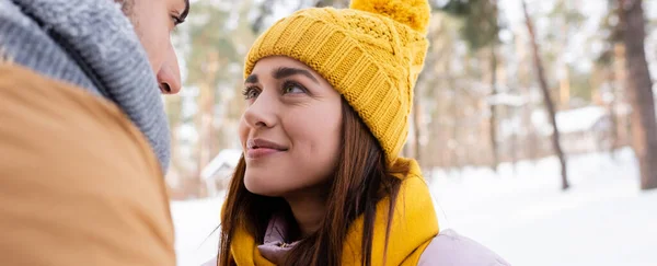 Mujer joven en sombrero de punto mirando novio en el parque de invierno, pancarta - foto de stock