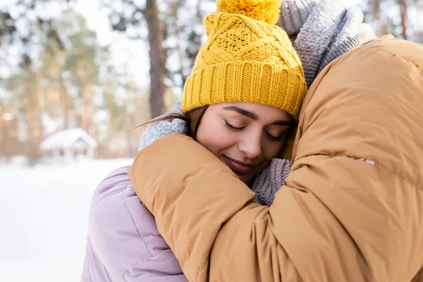 Man embracing young girlfriend in knitted hat in winter park — Stock Photo