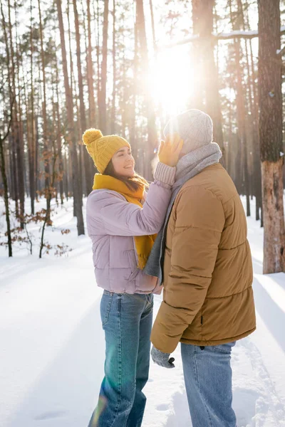 Mulher feliz em chapéu de malha tocando rosto de namorado no parque nevado — Fotografia de Stock