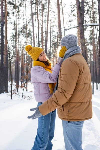 Jolie femme souriant tout en touchant le visage du petit ami dans le parc d'hiver — Photo de stock