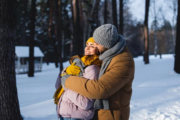 Мужчина в вязаной шляпе обнимает красивую девушку в зимнем парке — стоковое фото