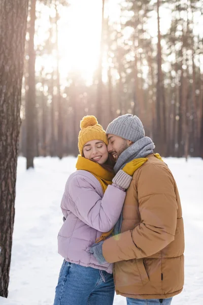 Улыбающийся мужчина с закрытыми глазами стоит рядом с девушкой в зимнем парке — стоковое фото