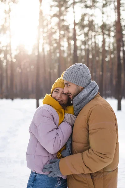 Jeune couple positif regardant loin dans un parc enneigé — Photo de stock