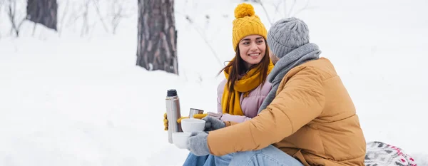 Donna con thermos guardando fidanzato con tazze nella foresta invernale, banner — Foto stock