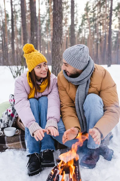 Улыбающаяся пара разогревает руки у костра в зимнем парке — стоковое фото