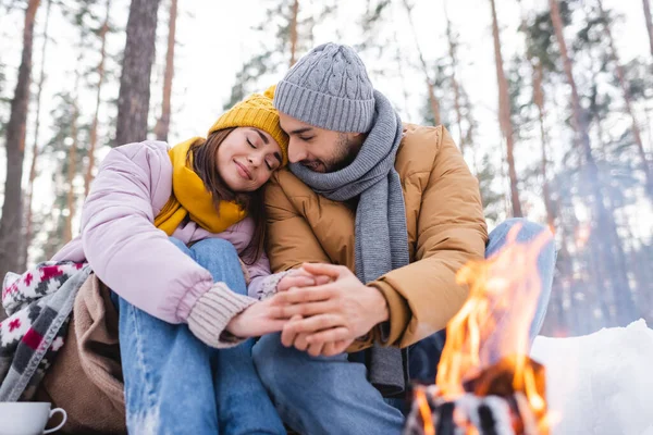 Jeune couple tenant la main près de feu de joie dans le parc d'hiver — Photo de stock