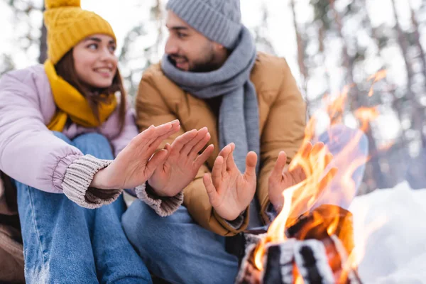 Lagerfeuer bei verschwommenem Paar wärmt Hände im Winterpark — Stockfoto