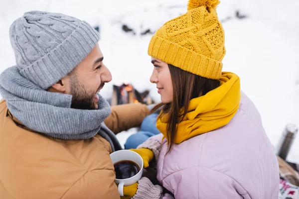 Vista lateral do homem alegre olhando para a namorada com xícara de café no parque de inverno — Fotografia de Stock