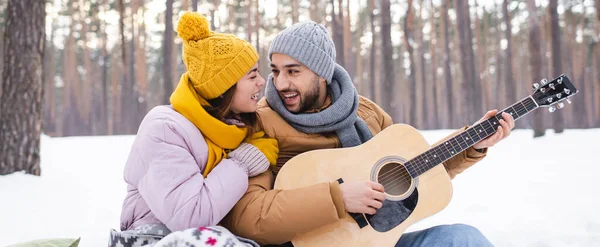 Coppia allegra in abito invernale suonare la chitarra acustica nel parco, banner — Foto stock