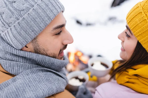 Улыбающаяся пара в вязаных шляпах, смотрящая друг на друга в зимнем парке — стоковое фото