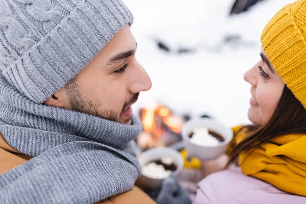 Pareja sonriente en sombreros de punto mirándose en el parque de invierno - foto de stock