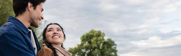 Sonriendo mujer asiática mirando novio durante fin de semana al aire libre, bandera - foto de stock