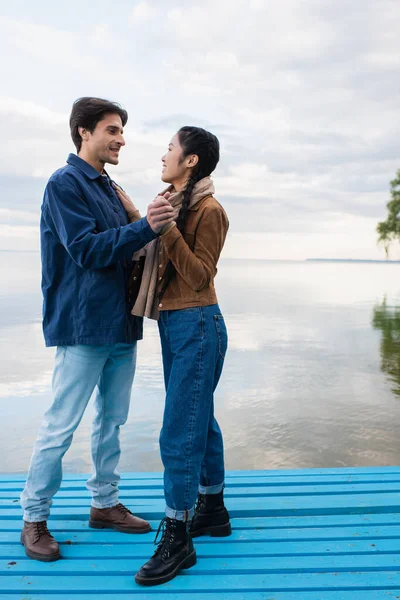 Side view of interracial couple holding hands on pier near lake — Stock Photo