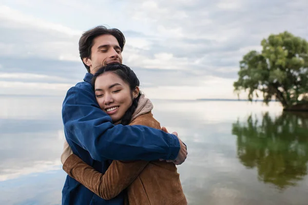 Чоловік обіймає азіатську дівчину біля озера — стокове фото