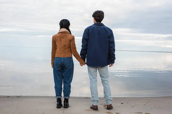 Vista trasera de pareja cogida de la mano en la orilla cerca del mar - foto de stock