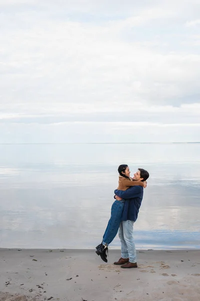 Seitenansicht eines multiethnischen Paares, das sich am Strand am Meer umarmt — Stockfoto