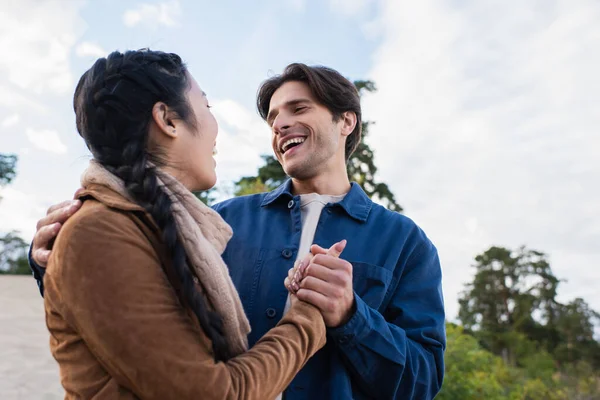 Tiefansicht eines fröhlichen Mannes, der am Wochenende die Hand seiner asiatischen Freundin hält — Stockfoto