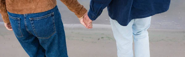 Vista recortada de pareja joven cogida de la mano en la playa, pancarta - foto de stock