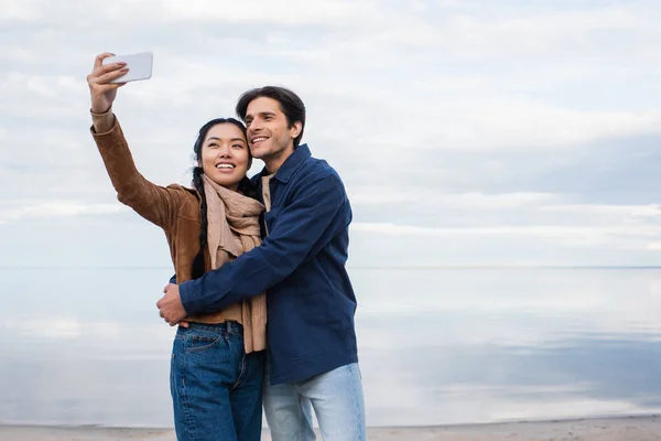 Asian woman taking selfie with boyfriend on beach — Stock Photo