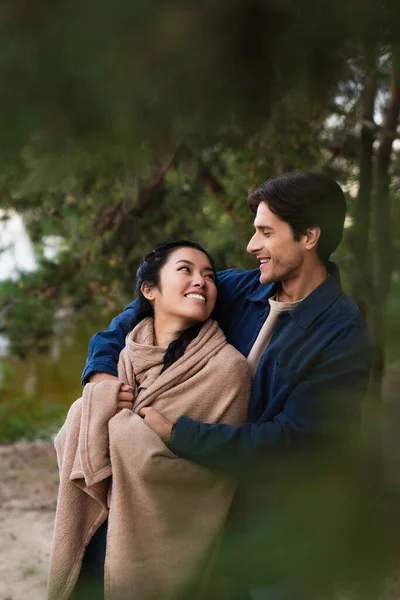 Couple interracial souriant avec couverture se regardant à l'extérieur — Photo de stock