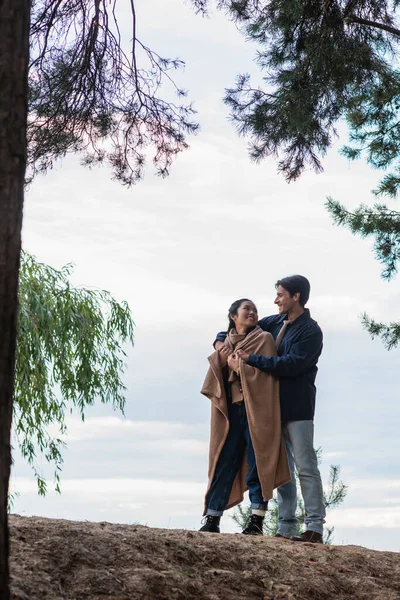 Man hugging asian girlfriend in blanket on hill outdoors — Stock Photo