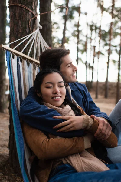 Hombre abrazando asiático mujer en hamaca al aire libre — Stock Photo