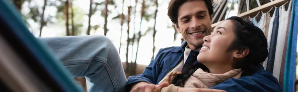 Sonriente pareja multiétnica descansando en hamaca en otoño, pancarta - foto de stock