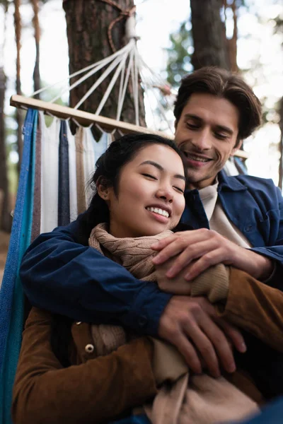 Verschwommener Mann umarmt asiatische Freundin in Hängematte im Herbst — Stockfoto