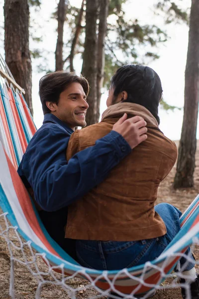 Smiling man hugging asian girlfriend in hammock outdoors — Stock Photo