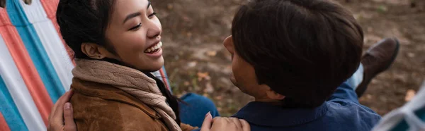 Mujer asiática sonriendo a novio en hamaca al aire libre, bandera - foto de stock
