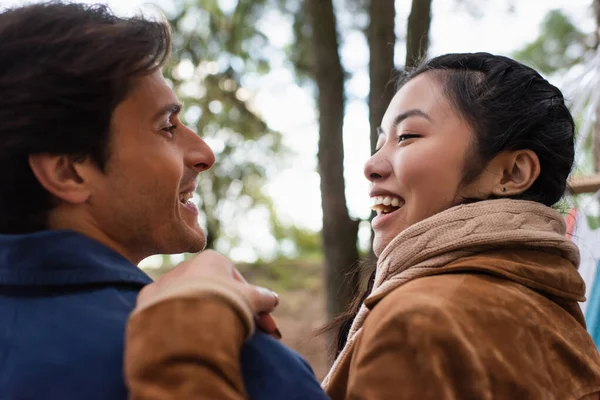 Positive asian woman hugging and looking at boyfriend outdoors — Stock Photo