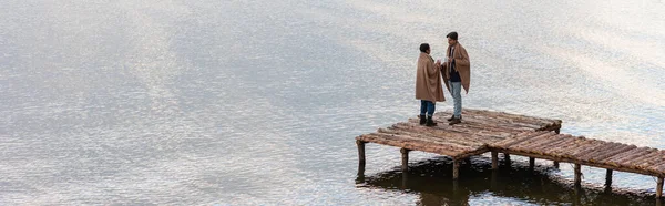 Jeune couple interracial avec des tasses debout sur la jetée près du lac, bannière — Photo de stock
