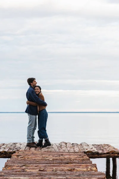 Feliz asiático mujer abrazando novio en madera muelle - foto de stock