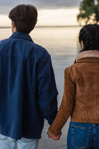 Vista trasera de la pareja cogida de la mano cerca del mar borroso - foto de stock