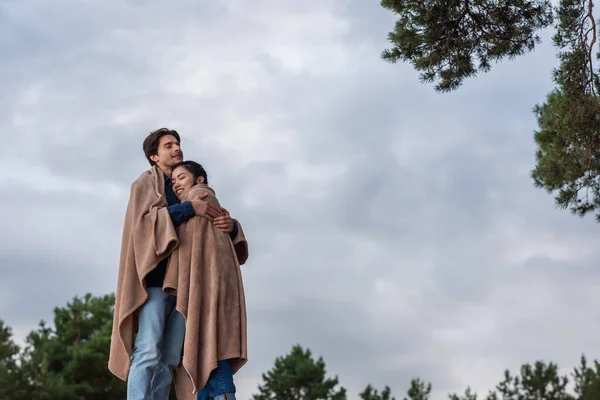 Man hugging asian girlfriend in blanket outdoors — Stock Photo