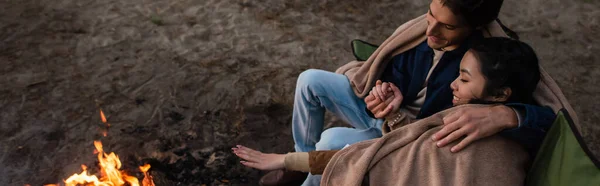 High angle view of interracial couple in blankets holding hands near campfire, banner — Stock Photo