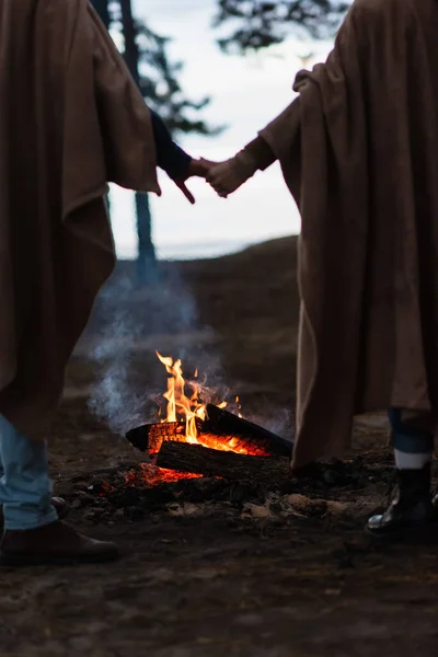 Vista cortada da fogueira perto de casal desfocado de mãos dadas à noite — Fotografia de Stock