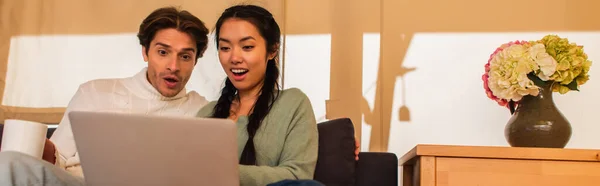 Excited interracial couple using laptop in glamping house, banner — Stock Photo