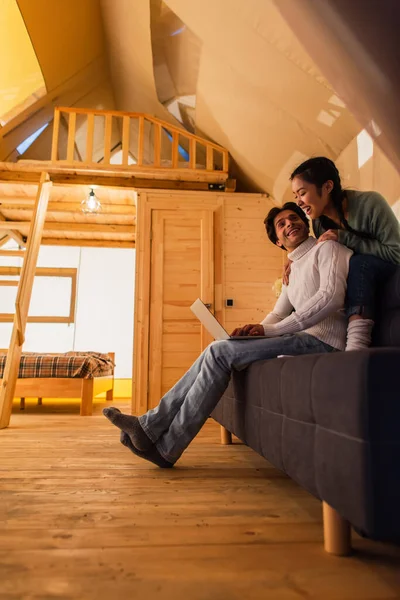 Cheerful interracial couple using laptop in wooden glamping house — Stock Photo