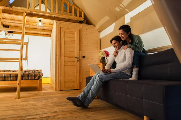 Multiethnic couple with laptop sitting on couch in glamping house — Stock Photo