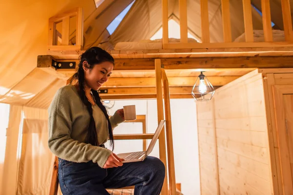 Smiling asian woman holding laptop in glamping house — Stock Photo