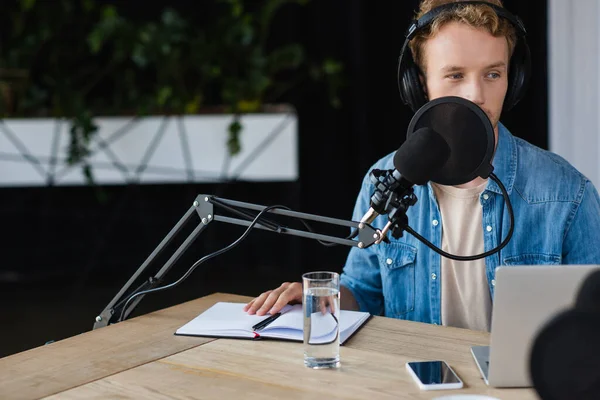 Influencer in cuffie parlando vicino a gadget e microfono in studio durante il podcast — Foto stock