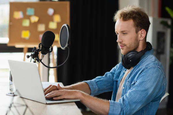 Radio host in headphones using laptop in studio — Stock Photo