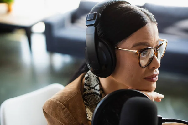 Asian radio host in glasses and headphones looking away during broadcast — Stock Photo