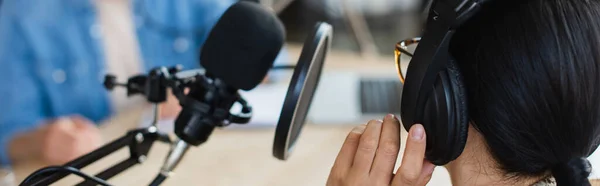 Radio host in glasses adjusting headphones near blurred colleague, banner — Stock Photo