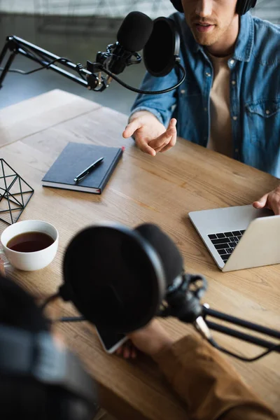 Cropped view of radio hosts talking in microphone during podcast — Stock Photo