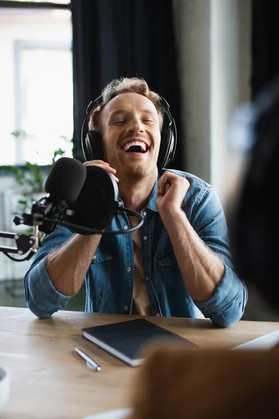 Радісний радіоведучий сміється біля мікрофона в студії — стокове фото