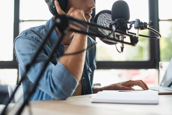 Vista recortada del anfitrión de radio ajustar los auriculares y hablar mientras se hace podcast - foto de stock